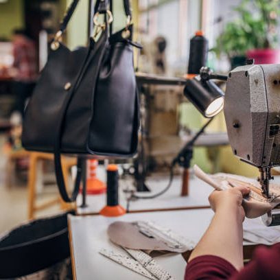 One mature woman working on sewing machine in workshop, making female leather purse.