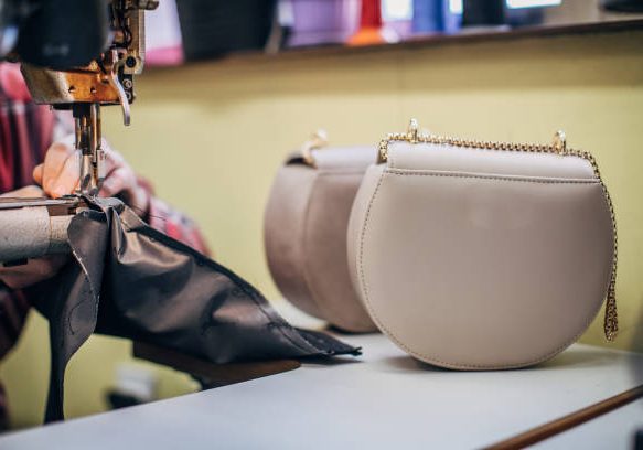 One mature man working on sewing machine in workshop, making female leather purse.
