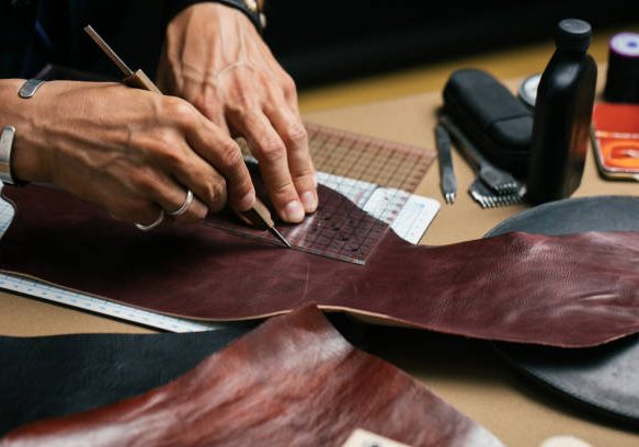 Close up of leather designer hands making custom made shoes working with genuine leather and hammer at a workshop.